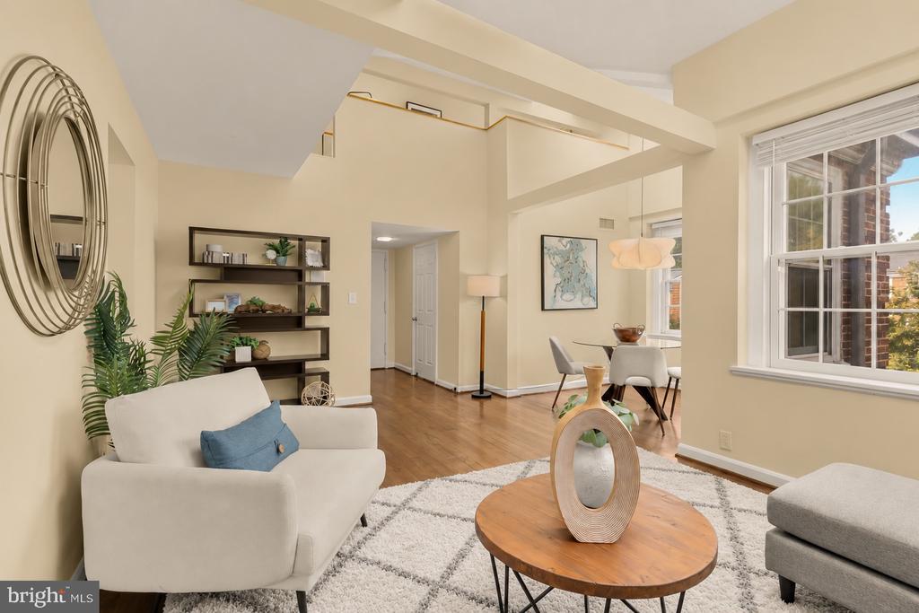 Living room with a white sofa, round wood coffee table, patterned rug, and open dining area.
