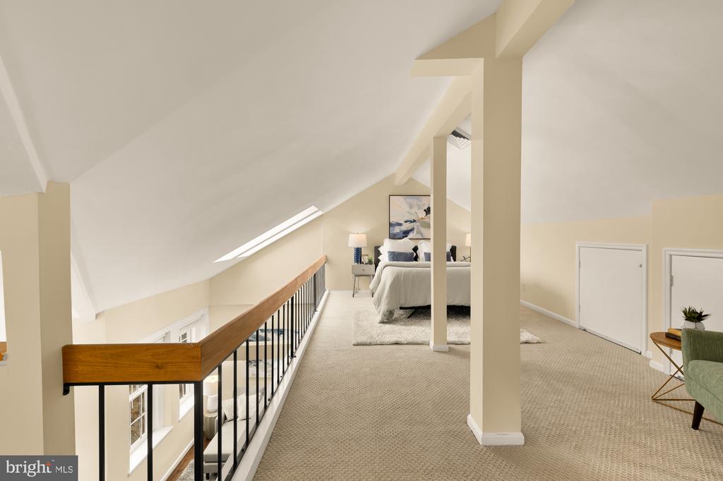 Furnished attic loft bedroom with a sloped ceiling, skylight, and railing overlooking the level below.