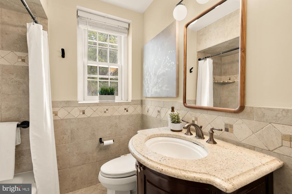 Bathroom with a curved wood vanity, stone countertop, and tiled shower.