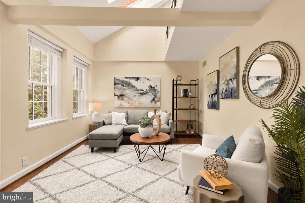 Staged living room with a gray sectional, white armchair, large windows, and abstract artwork.