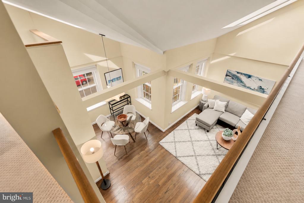 Open living and dining area with vaulted ceiling, hardwood floors, tall windows, and a gray sectional.