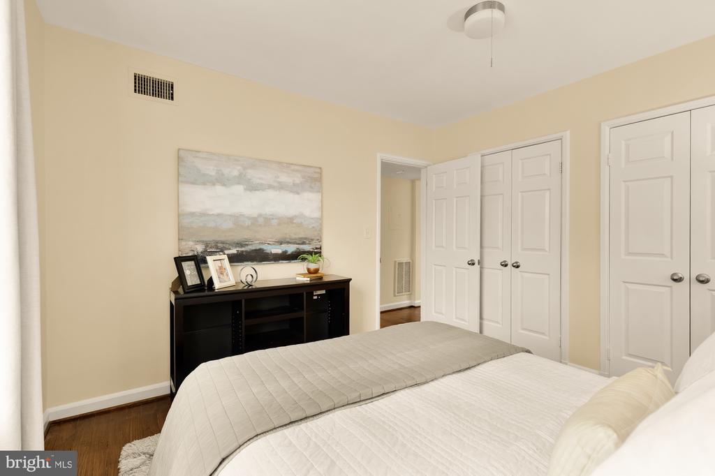 Furnished bedroom with white bedding, a black console, abstract wall art, and white closet doors.