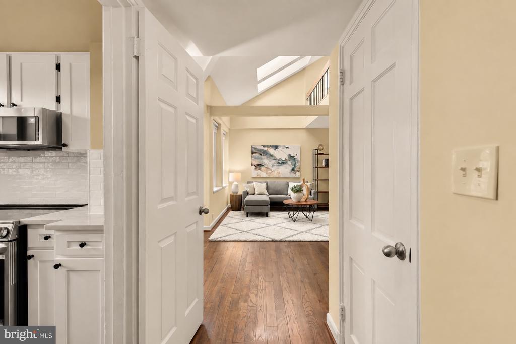 Hallway opens onto a furnished living room with a gray sofa and skylight; part of the kitchen is visible.