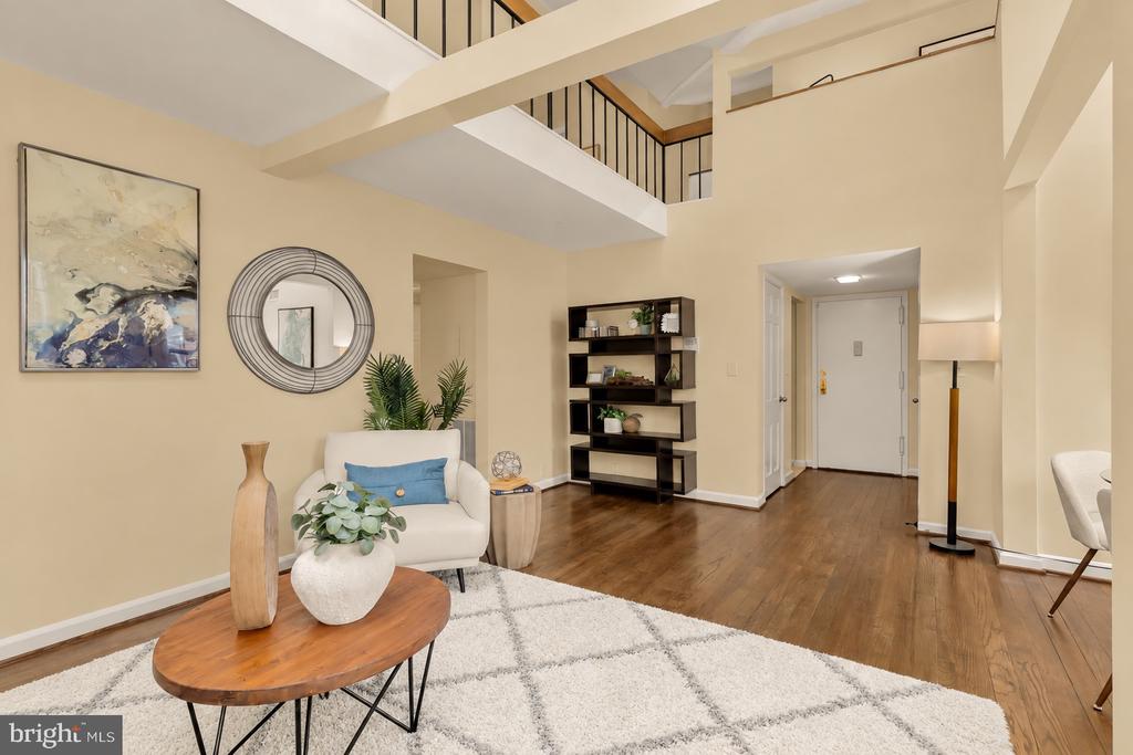 Staged living room with a double-height ceiling, loft railing, and hardwood floors.