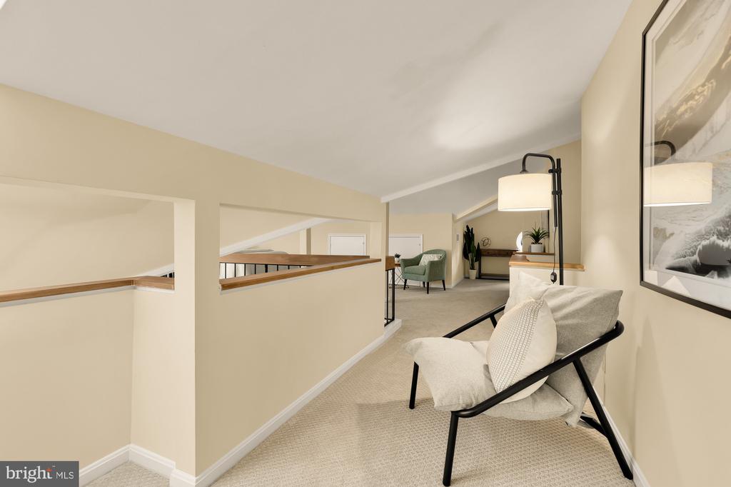Upstairs sitting area with a black-framed lounge chair, floor lamp, and green armchair.