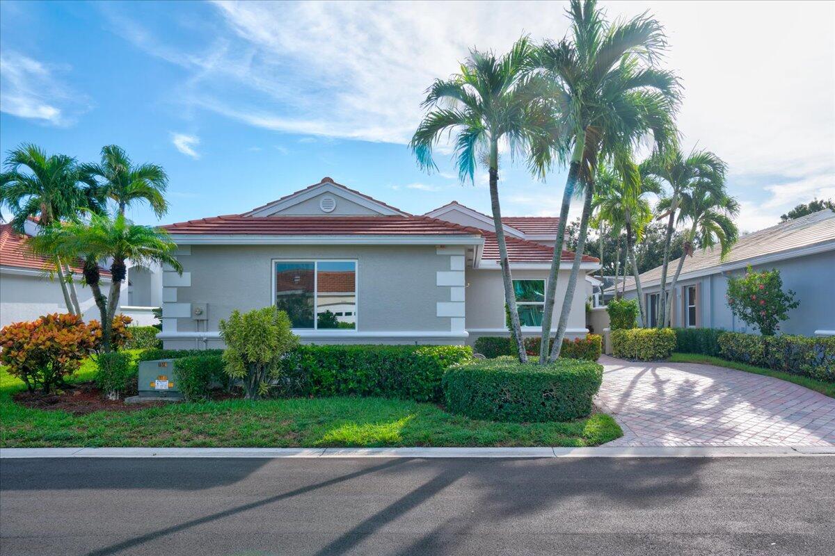 Single-story gray stucco home with a red tile roof, palm trees, and a curved paver driveway.