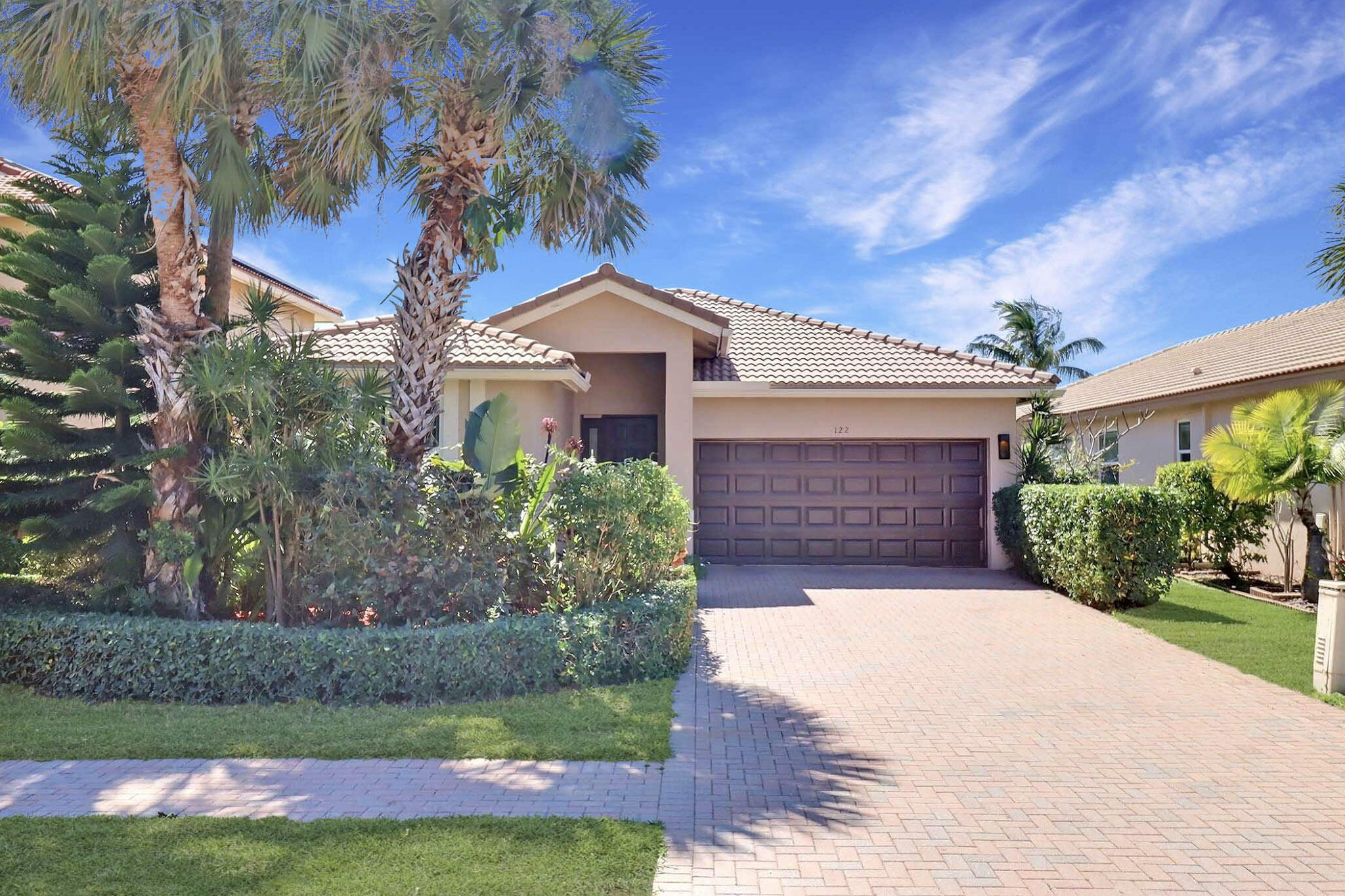 Stucco home with a tiled roof, double garage, paver driveway, and palm-lined landscaping.