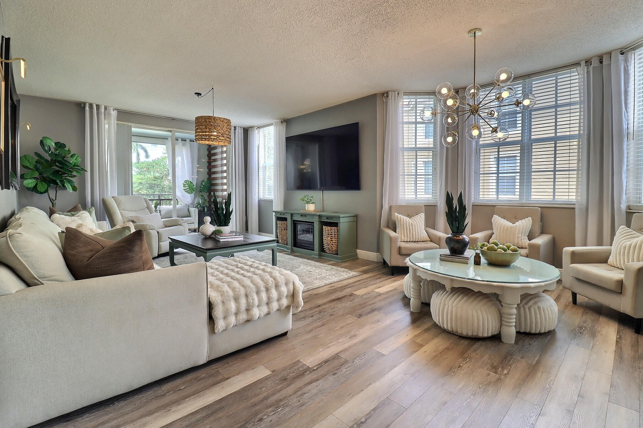 Furnished living room with cream seating, wood floors, and large windows with blinds.