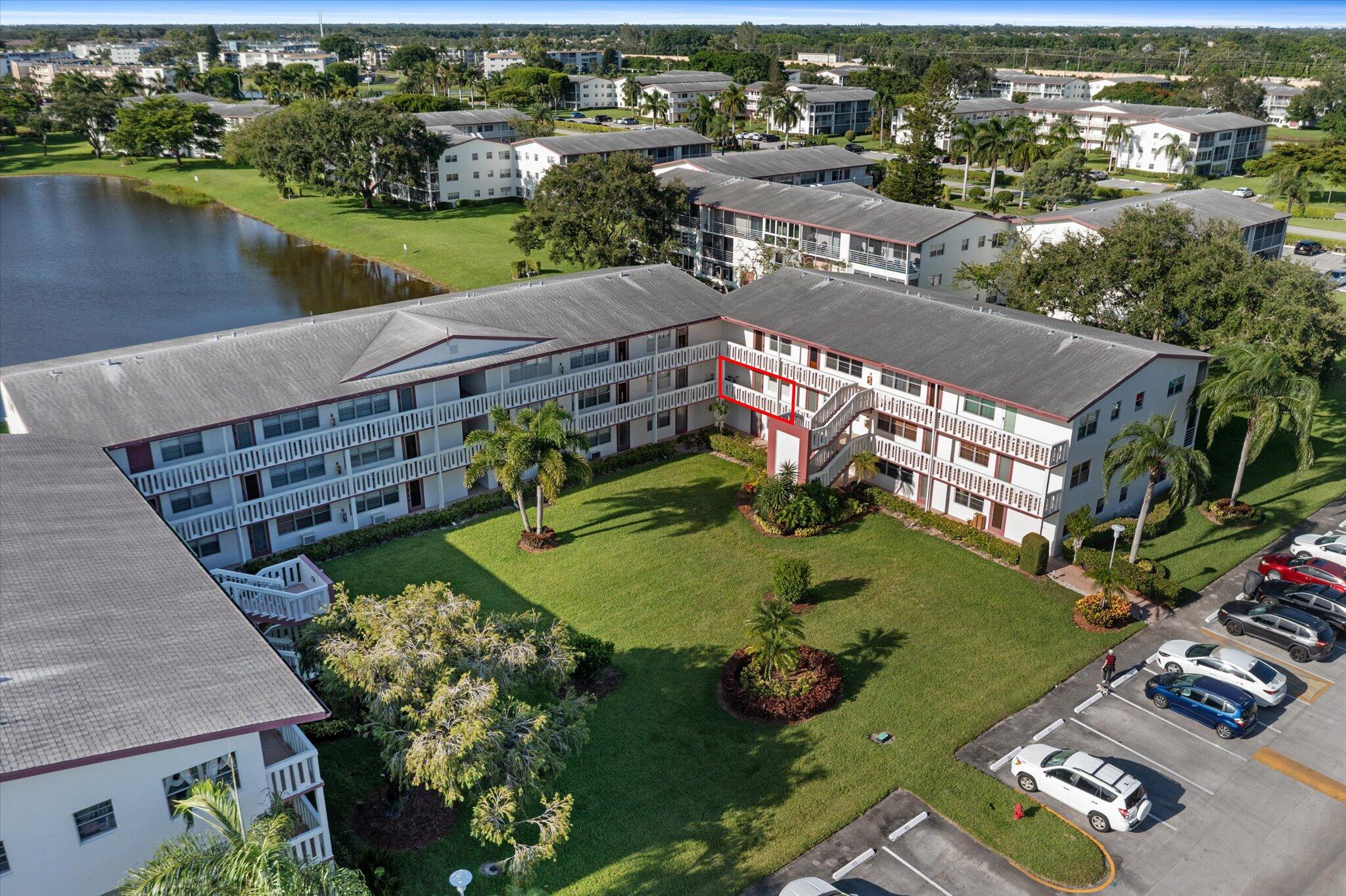 Aerial view of a condominium complex with a courtyard and lake; a red outline marks one balcony unit.
