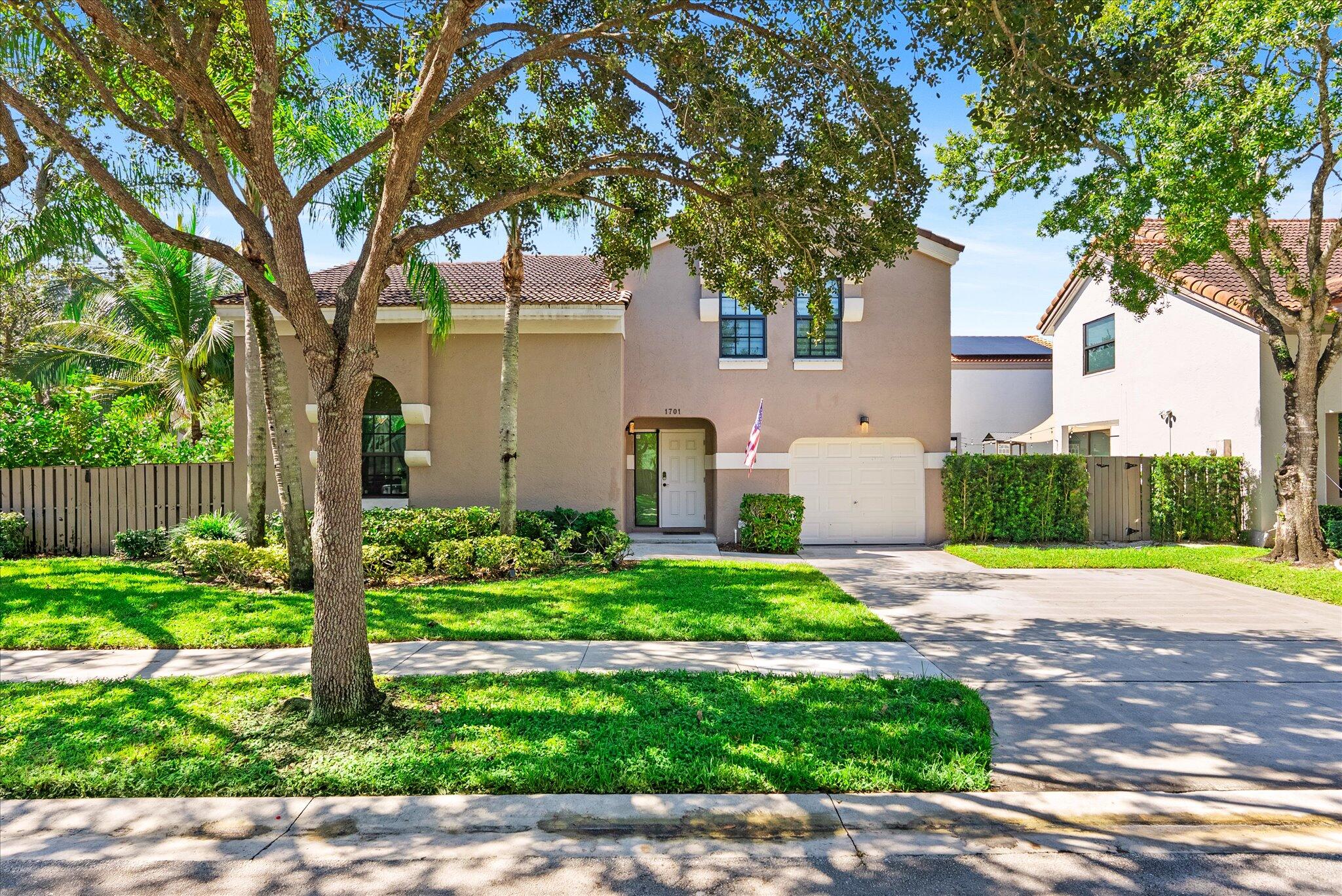 Two-story stucco home with a tiled roof, attached garage, and mature trees shading the front lawn.