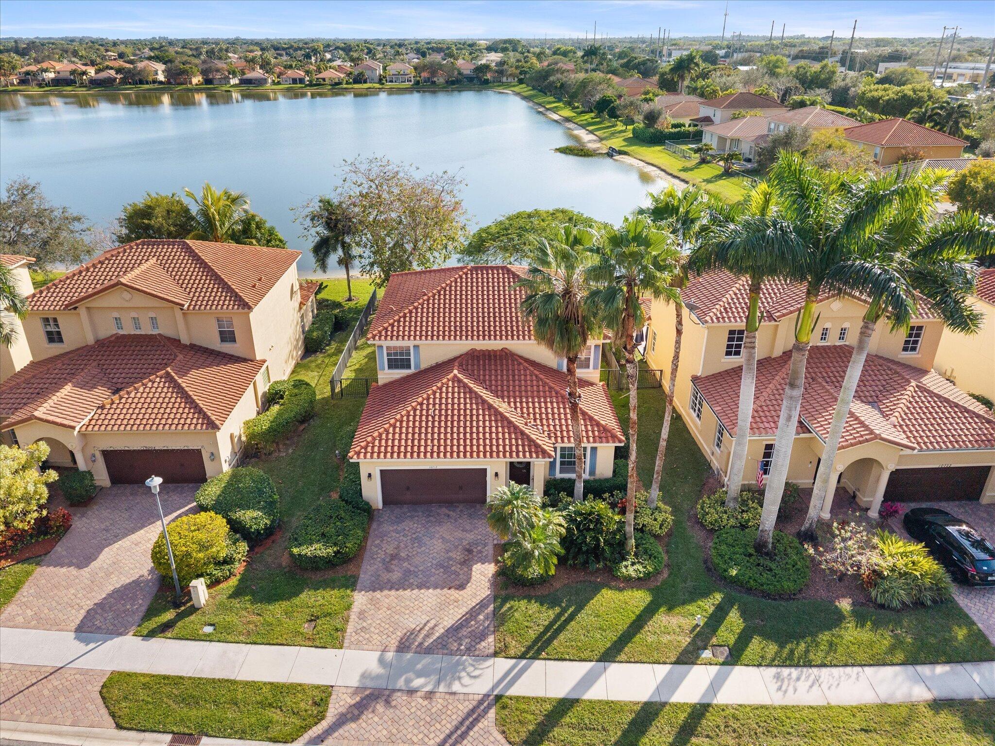 Aerial view of tile-roofed homes and palm trees beside a residential lake.