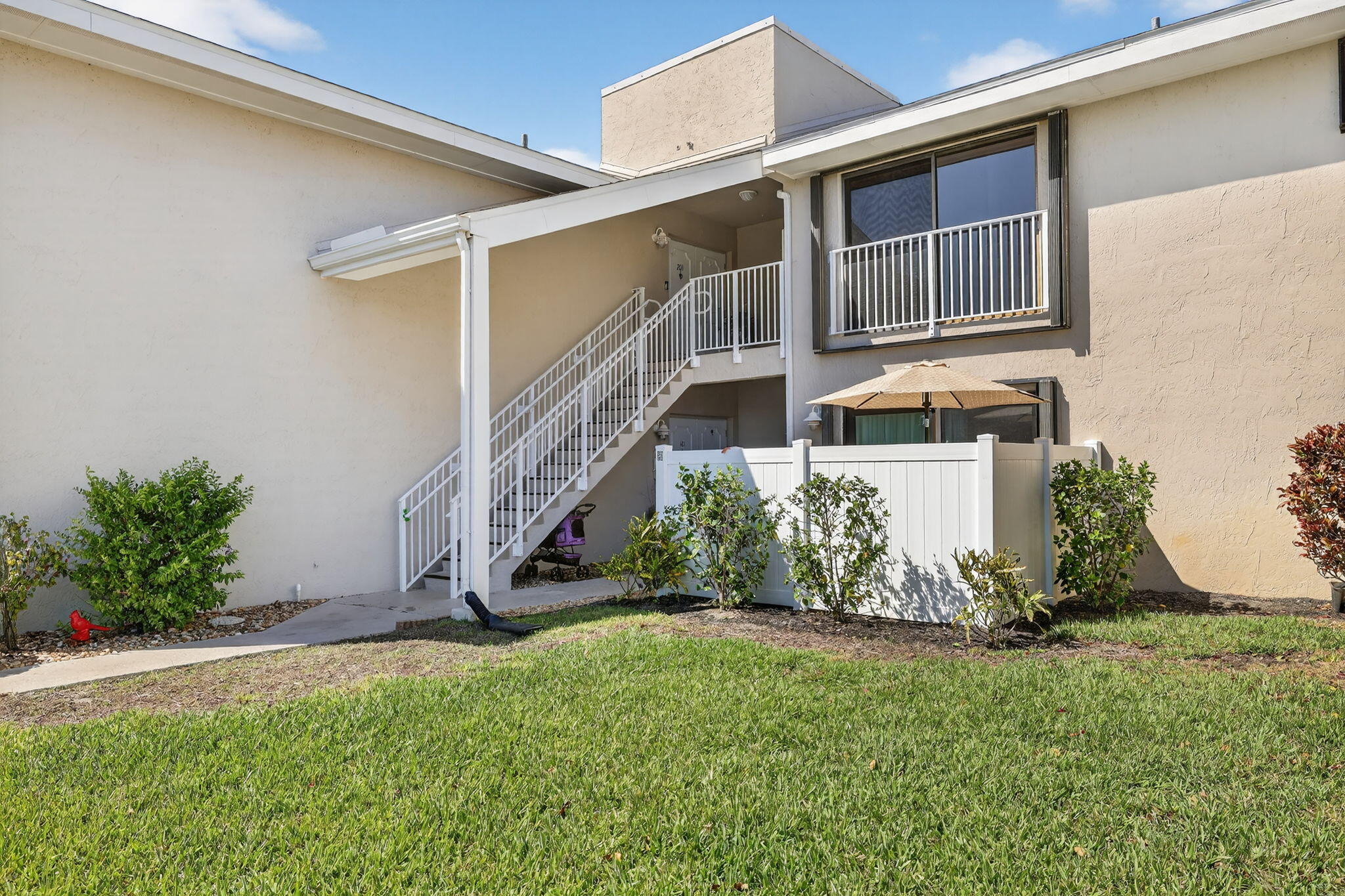 Condominium exterior with white-railed stairs, a fenced patio, and a grassy lawn.