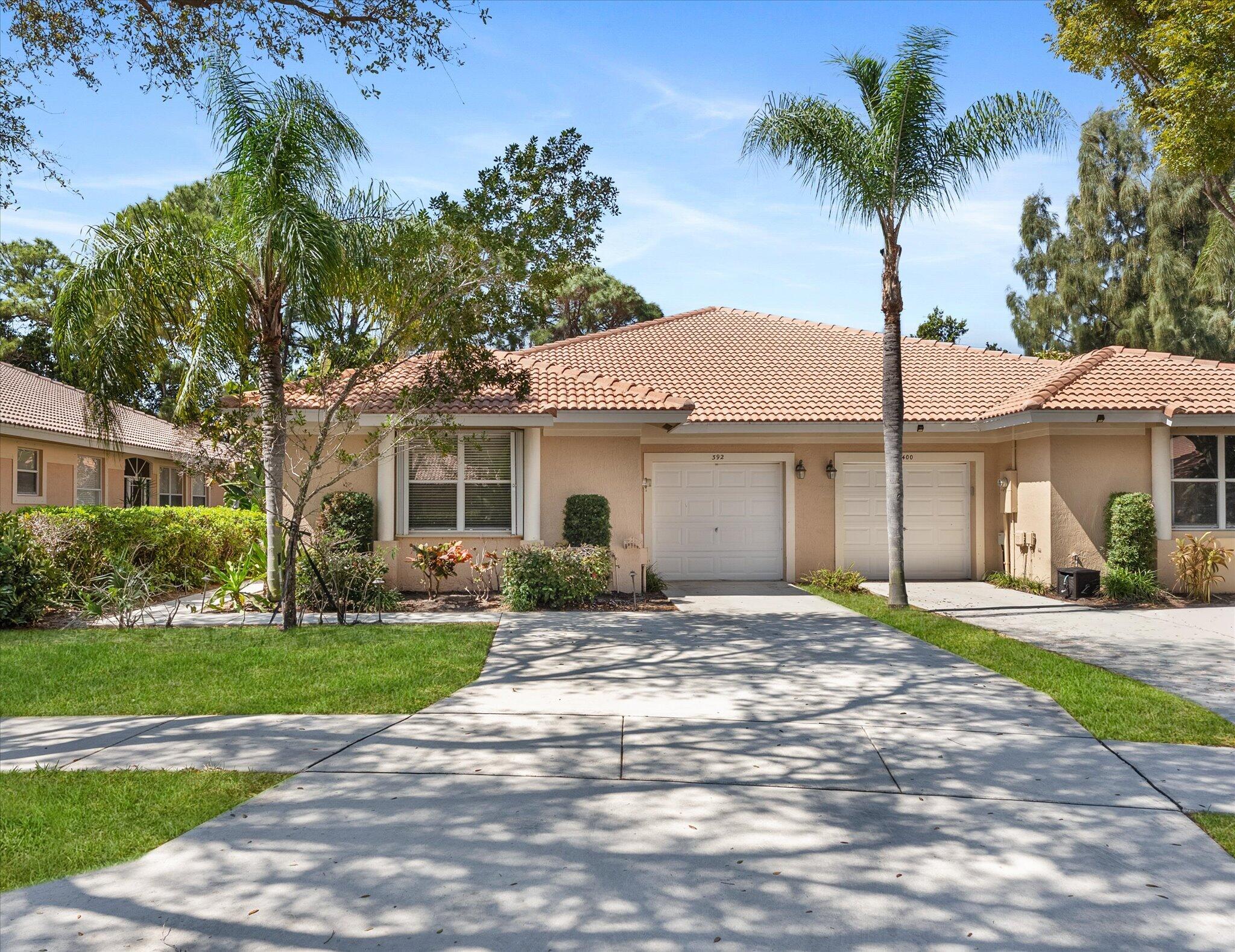 Single-story beige home with a terracotta tile roof, palm trees, and a wide driveway.