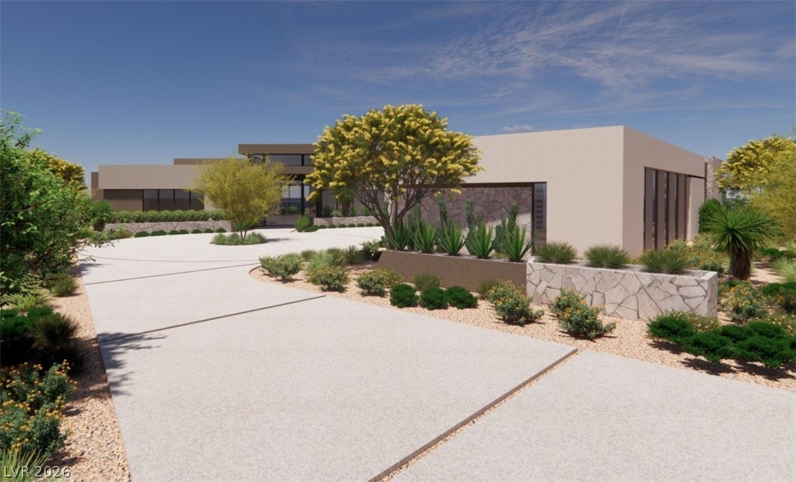 Modern home with flat roofs, stone accents, and desert landscaping along a broad driveway.