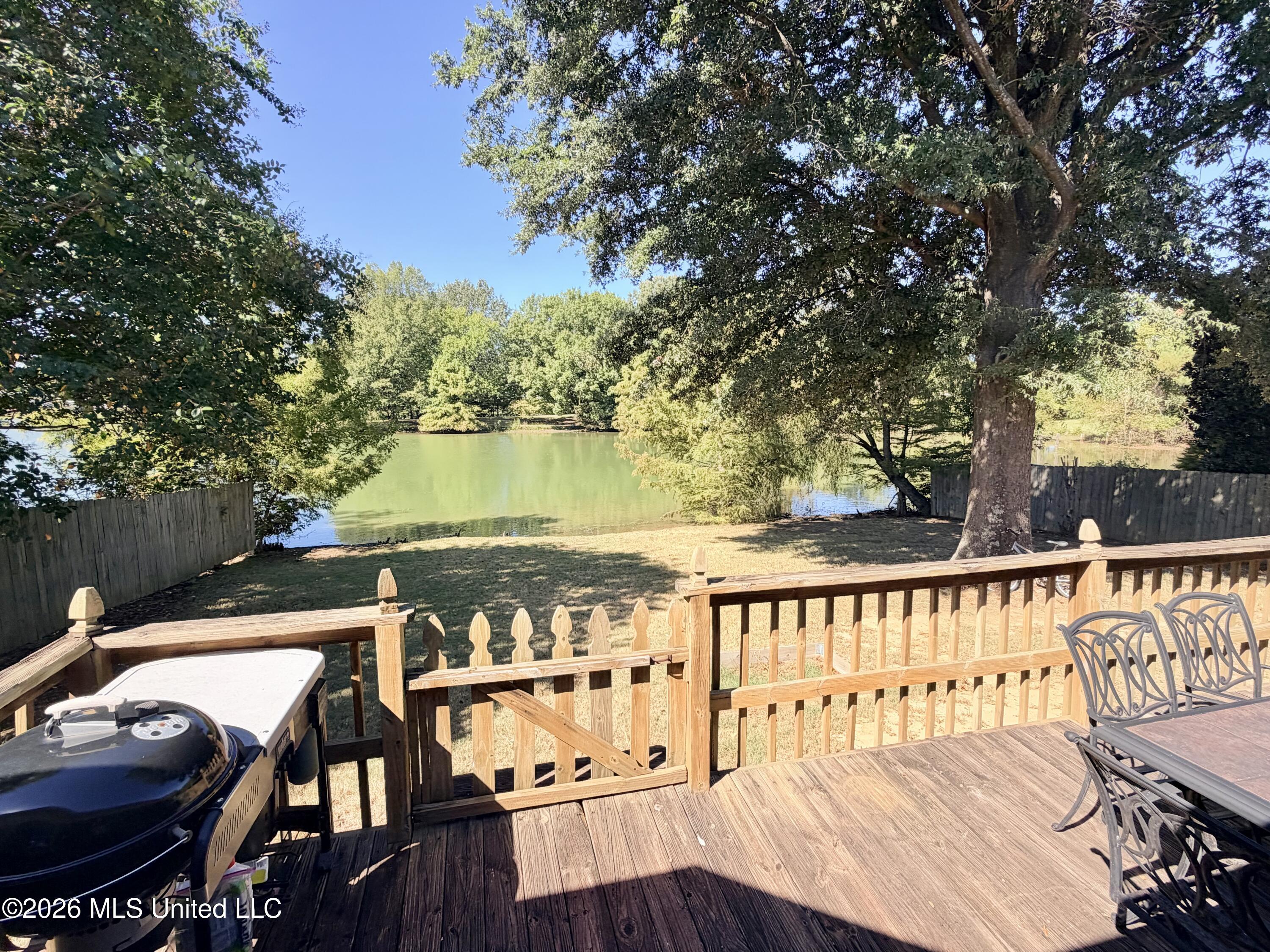 Wooden deck overlooking a tree-lined pond, with a grill and outdoor dining furniture.