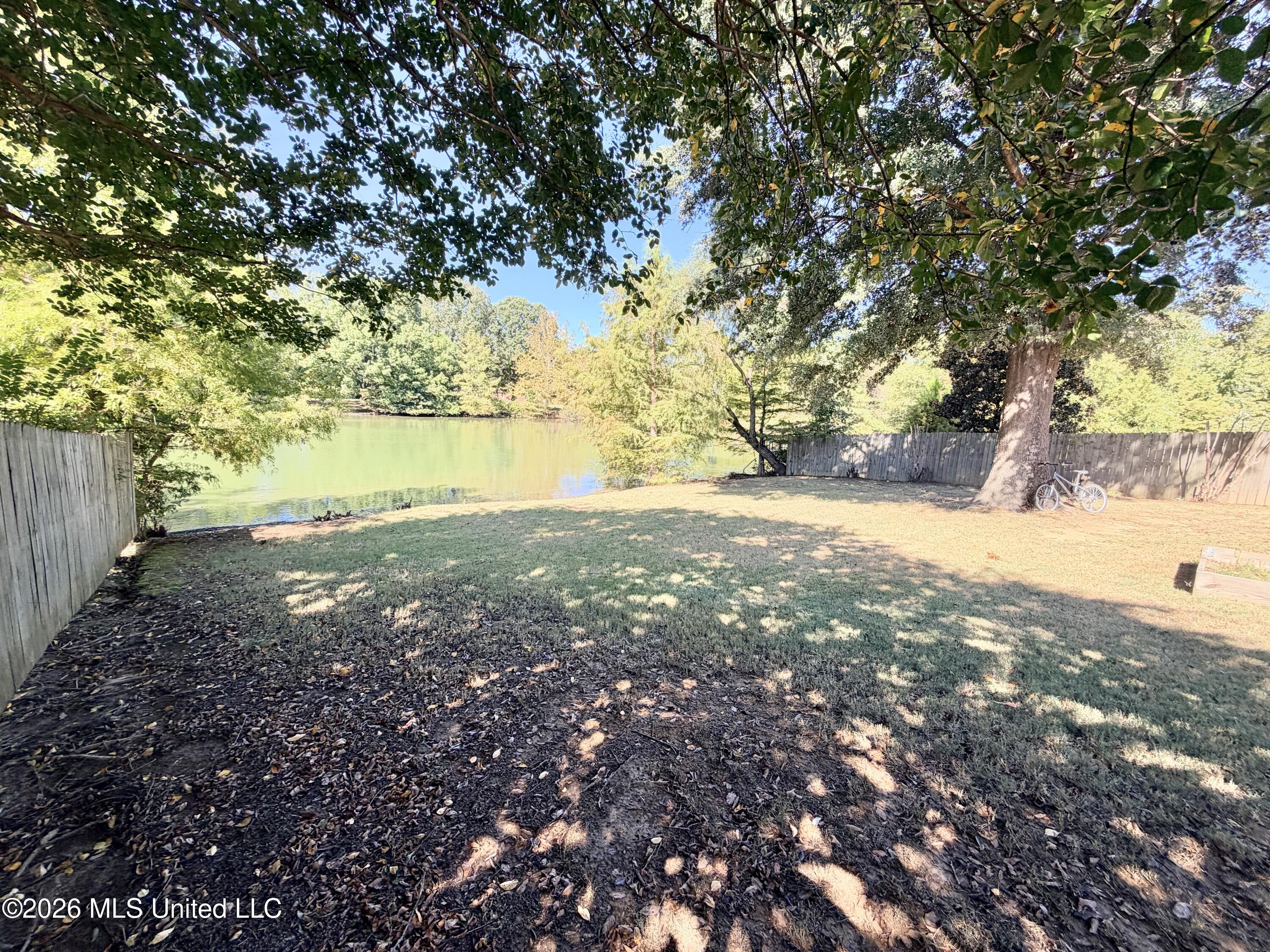 Fenced backyard with a pond, mature shade tree, and bicycle beside the fence.
