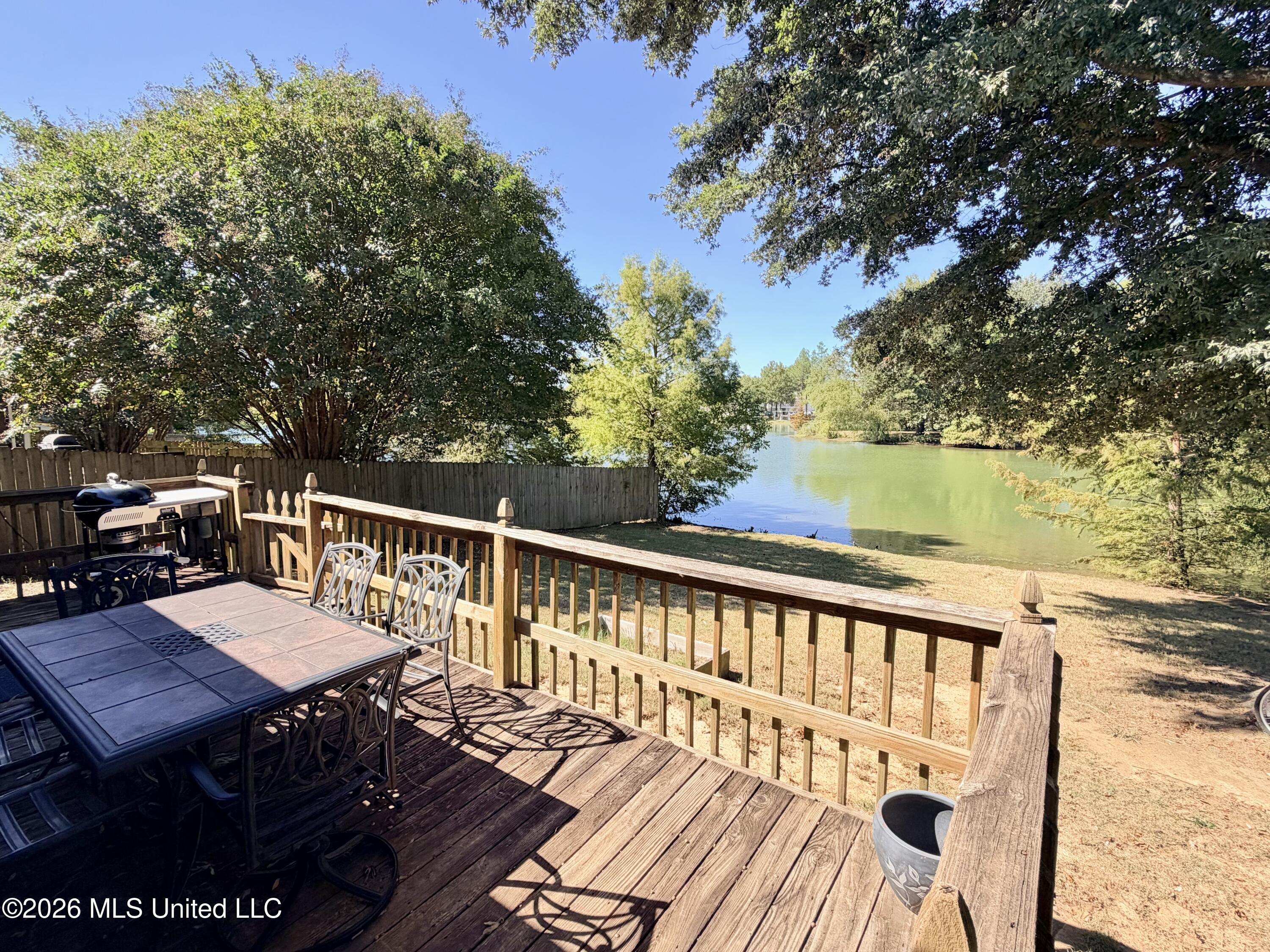 Wooden deck with outdoor dining set and grill overlooking a tree-lined lake.