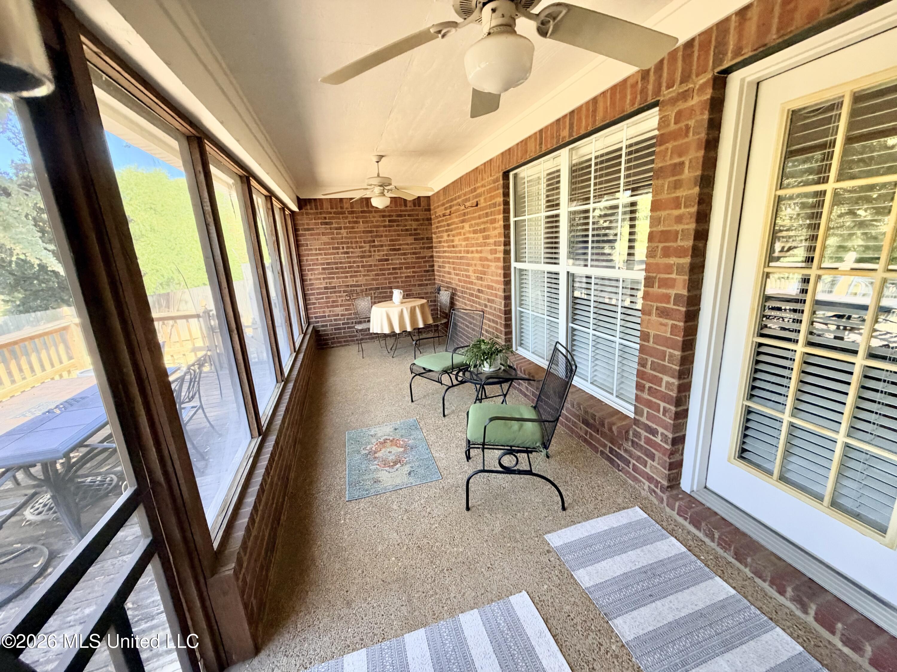 Brick sunroom with tall windows, ceiling fans, and seating with green cushions.