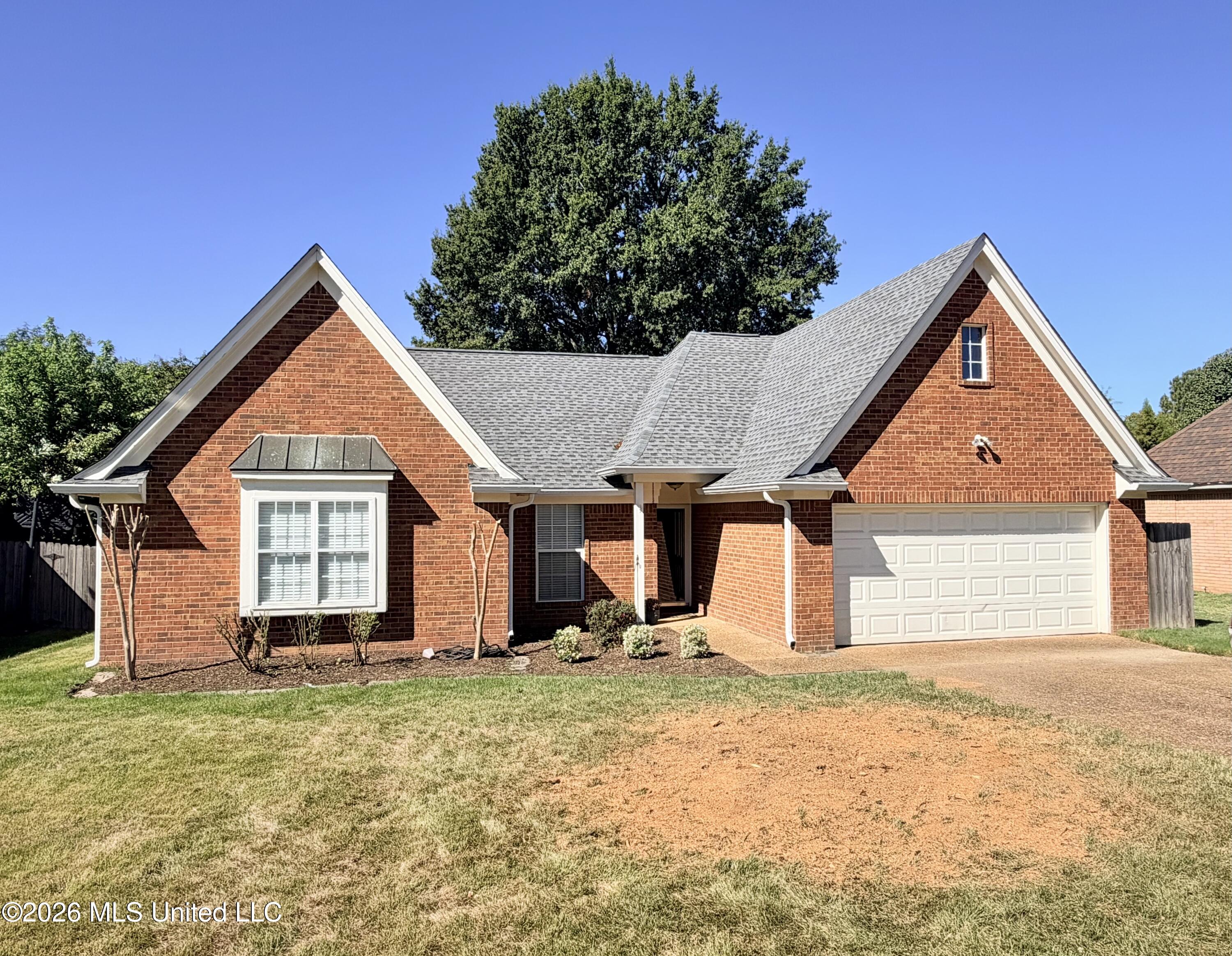 Red brick house with a gray gabled roof, attached garage, and broad front lawn.