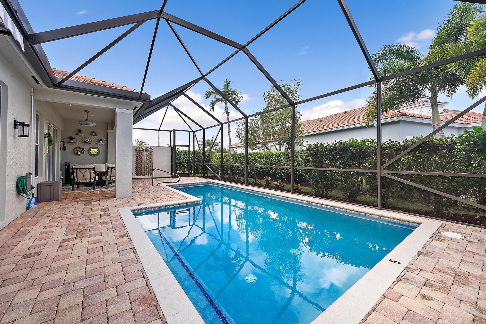 Backyard pool beneath a screened enclosure, beside a brick-paver deck and covered patio dining area.