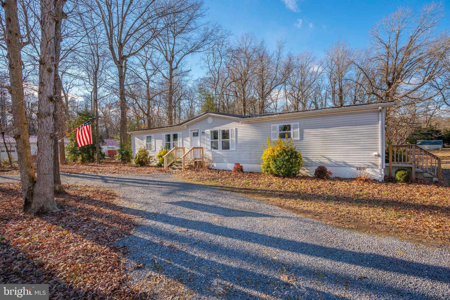 Light-gray single-story home with a small porch and gravel driveway beneath leafless trees.