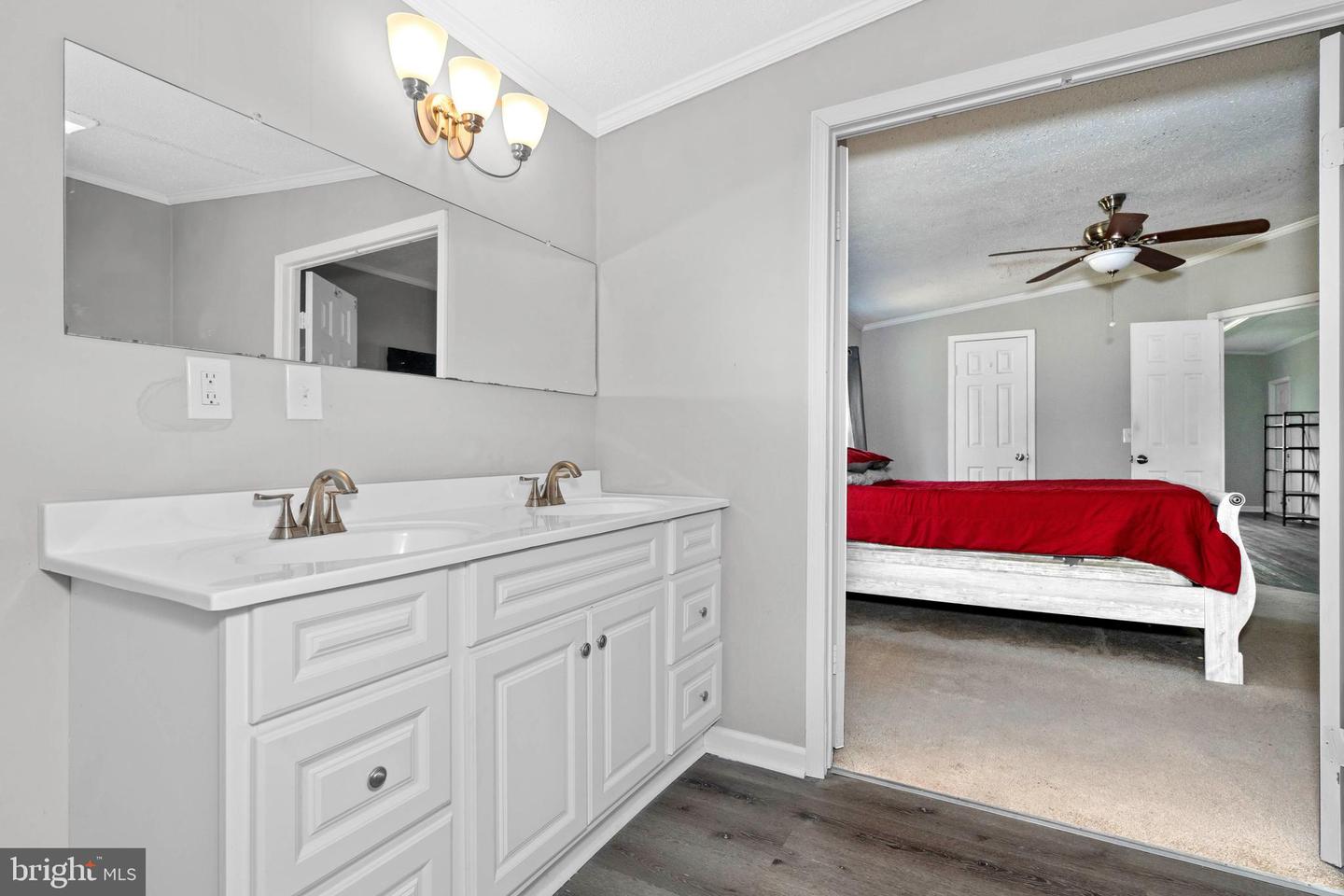 Double-sink bathroom vanity overlooking a bedroom with a white bed and red bedding.