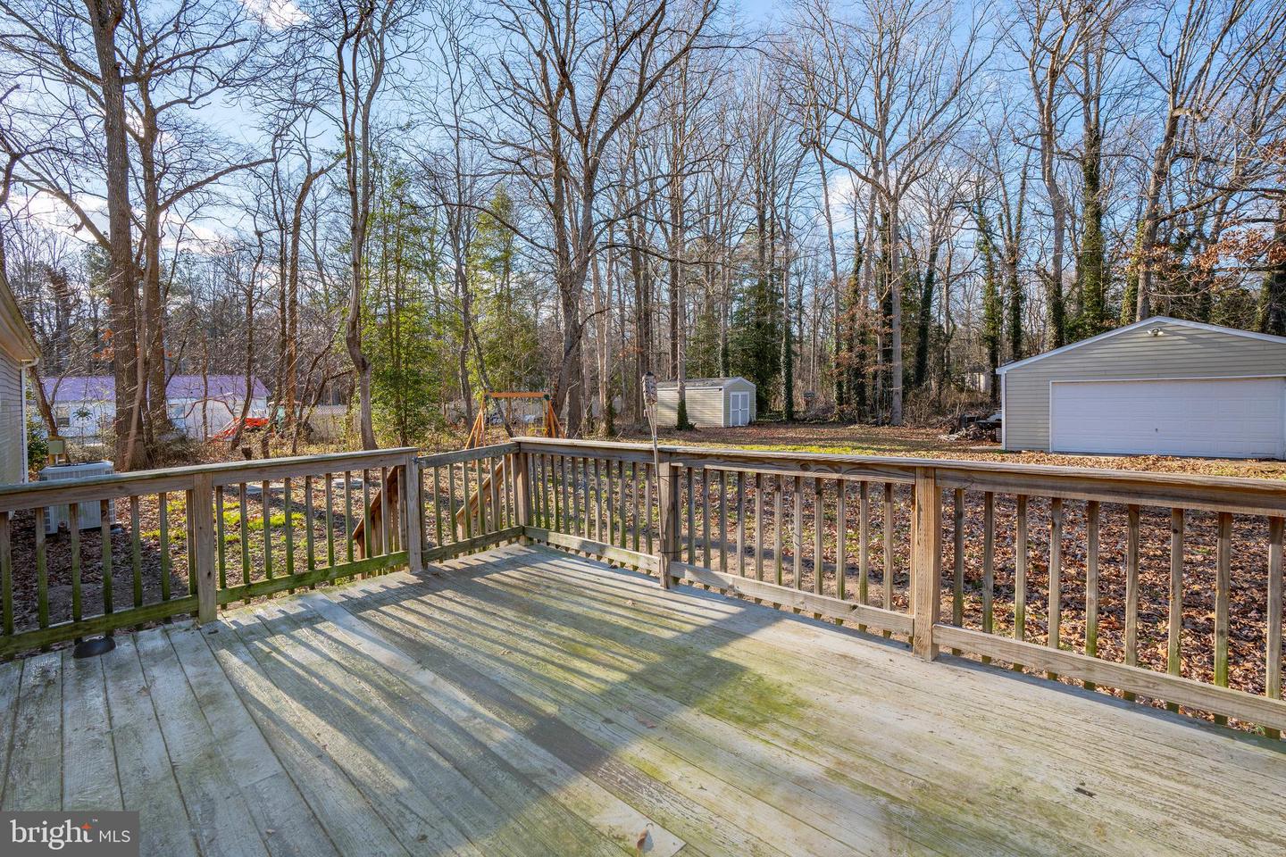 Wooden deck overlooking a wooded backyard with a detached garage and small shed.