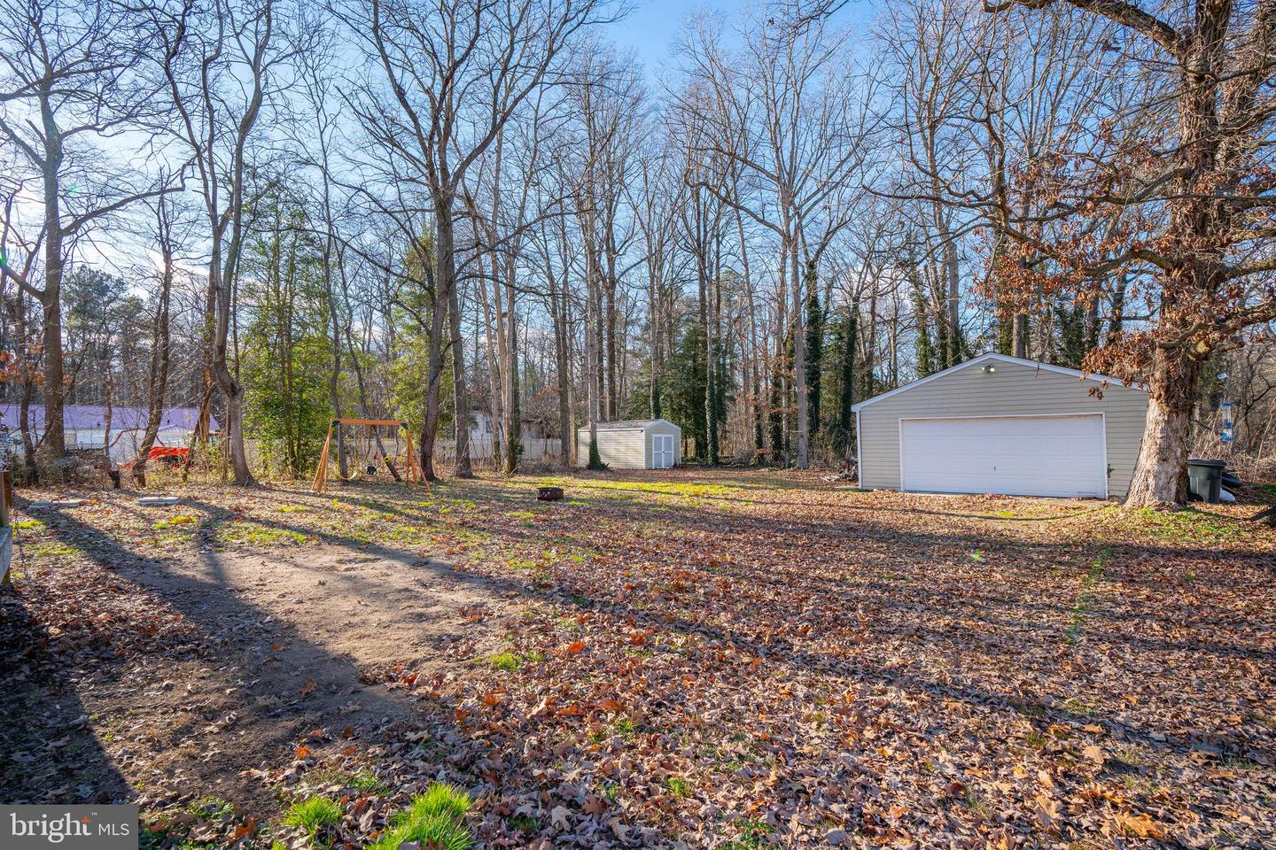 Wooded backyard with a detached garage, small shed, and swing set among bare trees.