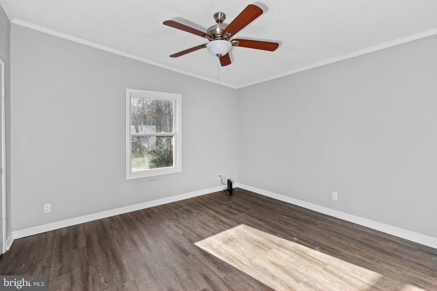 Empty bedroom with dark wood-look flooring, a window, and a wood-blade ceiling fan.