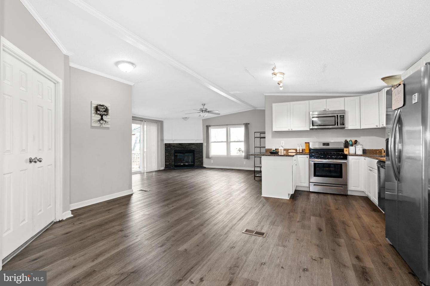 Open kitchen and living area with white cabinetry, stainless steel appliances, and a stone fireplace.
