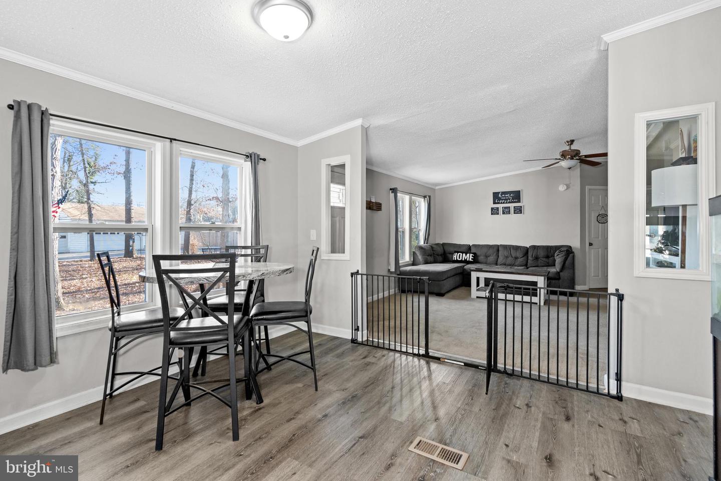 Dining and living area with large windows, gray flooring, a sectional sofa, and a black safety gate.