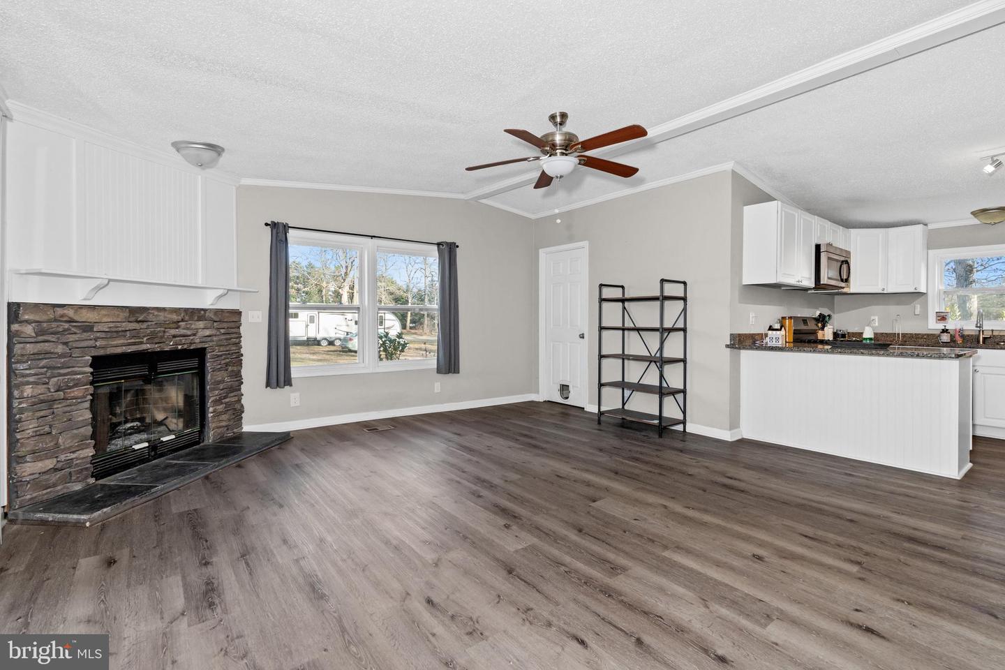 Living room opening to a kitchen, with a stone fireplace and gray wood-look flooring.