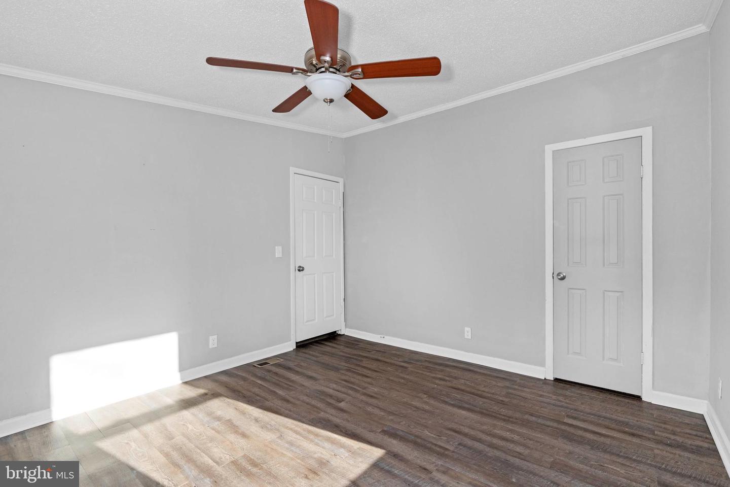 Empty bedroom with gray walls, dark flooring, two white doors, and a ceiling fan.