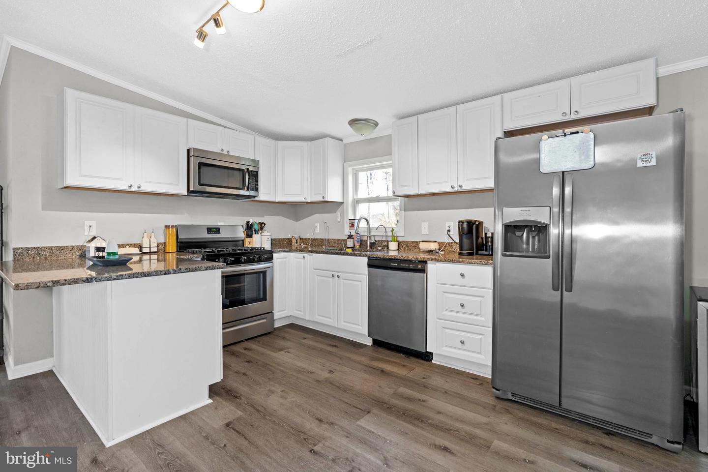 Kitchen with white cabinets, granite counters, stainless steel appliances, and a foreground peninsula.