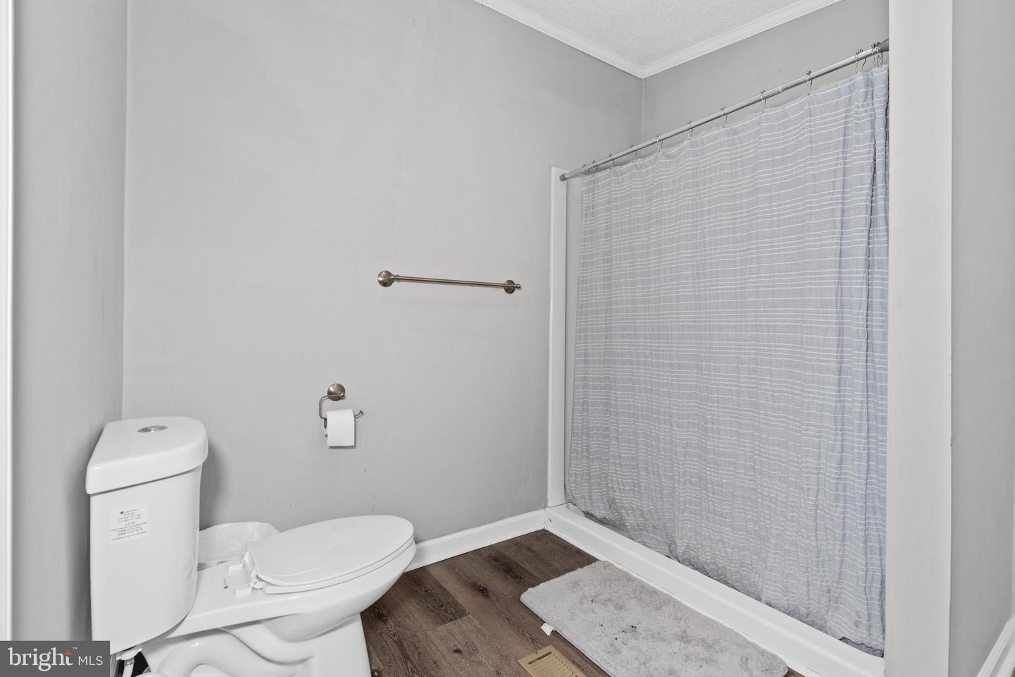 Bathroom with a white toilet, striped shower curtain, and dark wood-look flooring.