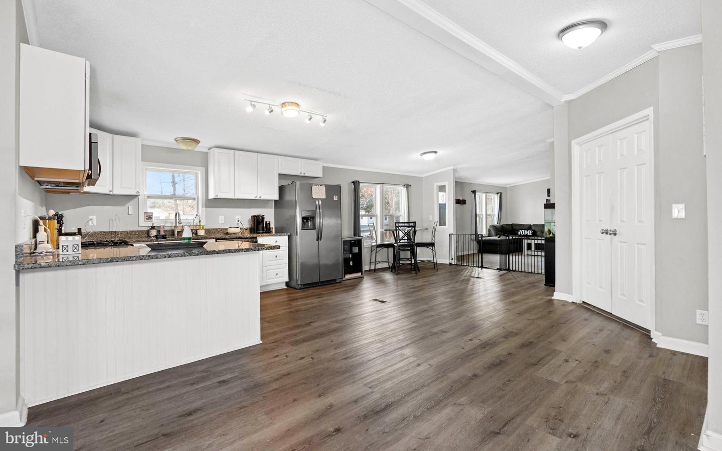 Open-plan kitchen with white cabinets and granite counters, adjoining a dining area and furnished living room.