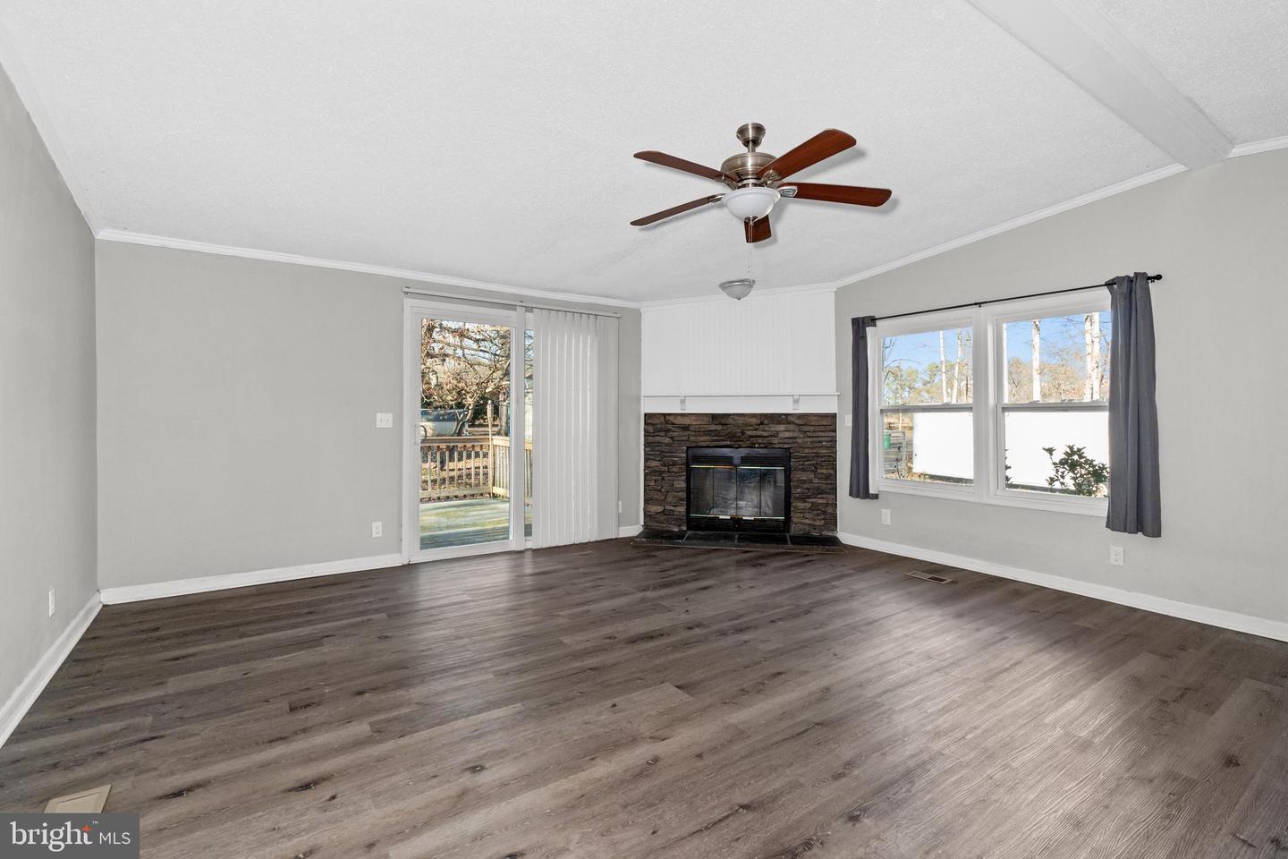 Vacant living room with a stone fireplace, dark flooring, and a sliding glass door.