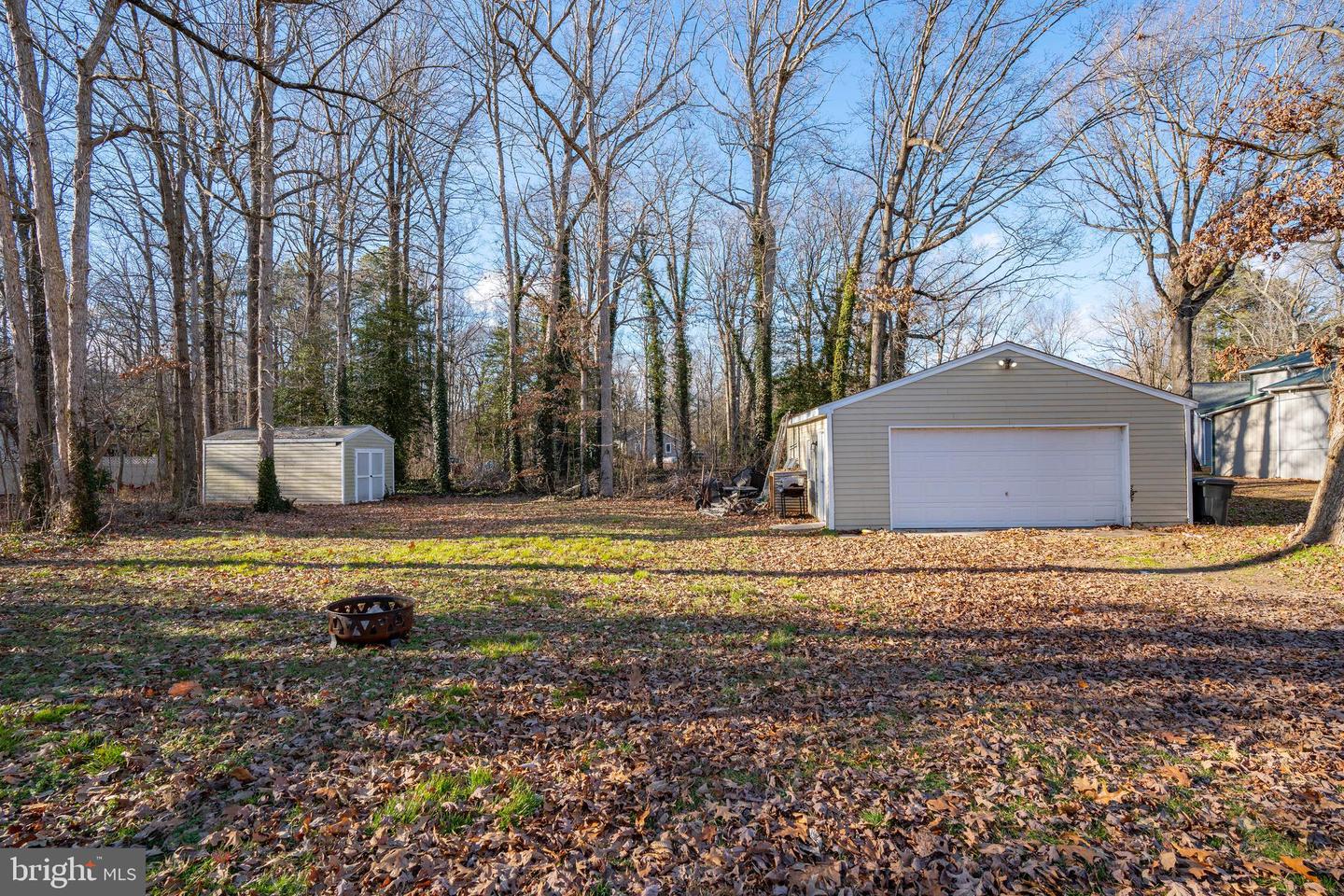 Detached garage and storage shed in a leaf-covered wooded backyard.
