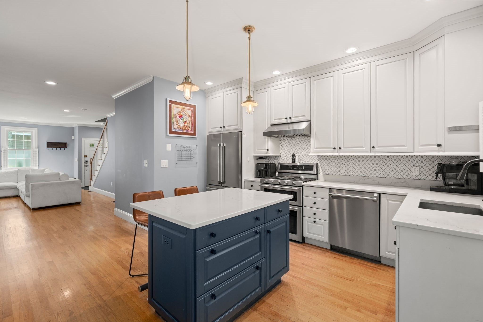 Open-plan kitchen with a navy island, white cabinetry, stainless steel appliances, and adjoining living area.