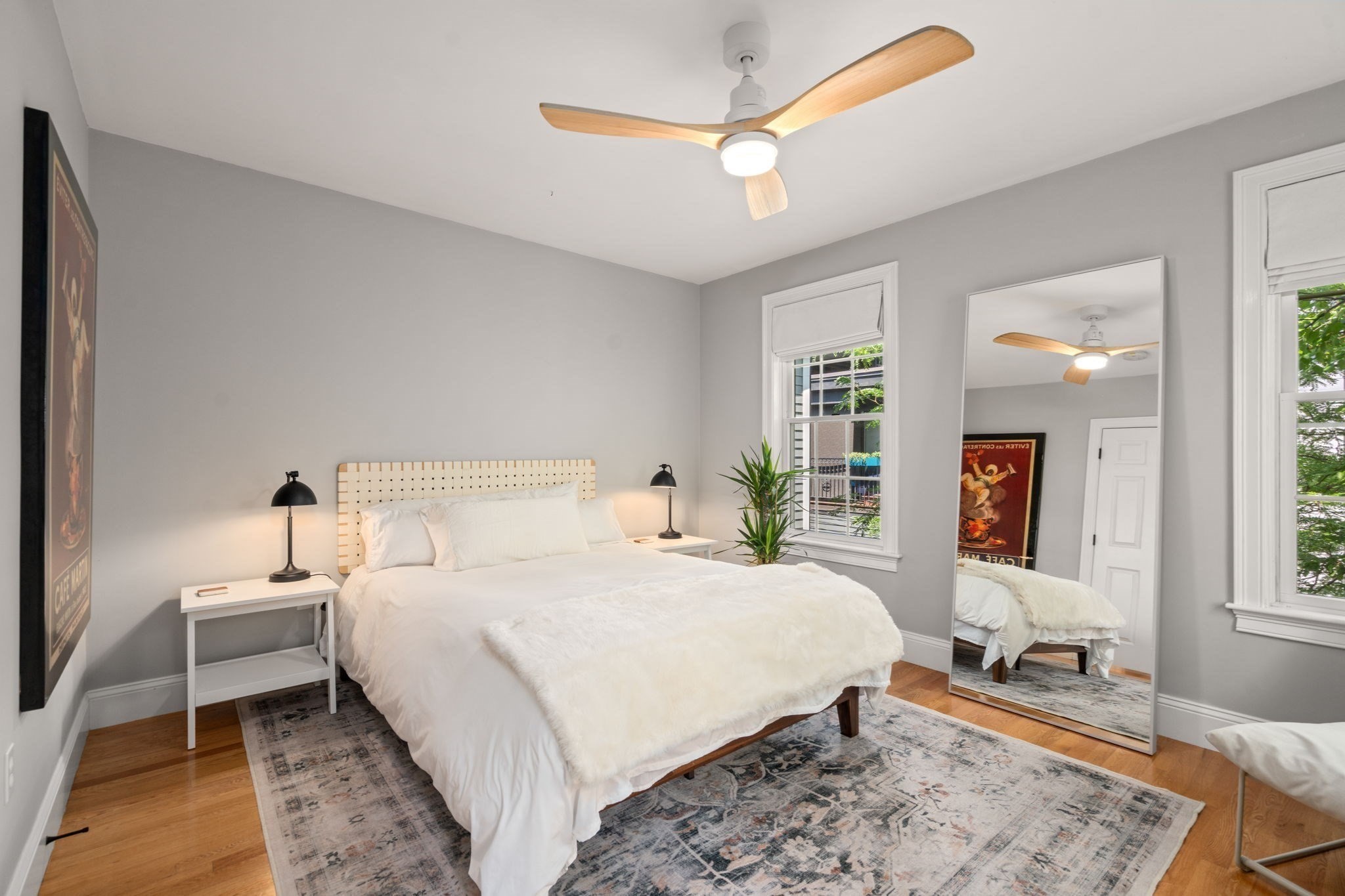 Bedroom with a white bed, pale wood headboard, patterned rug, and wood-bladed ceiling fan.