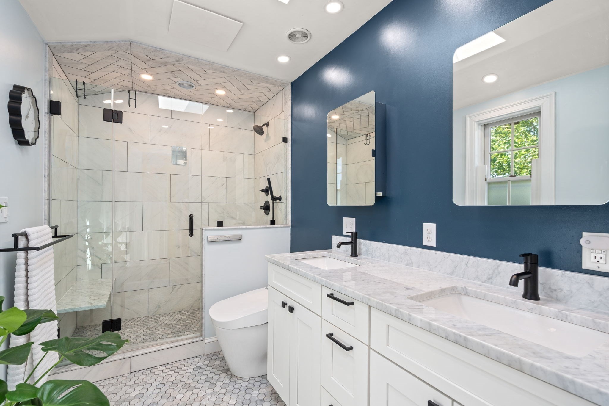 Bathroom with a glass walk-in shower, marble-look tile, and a white double vanity against a navy wall.