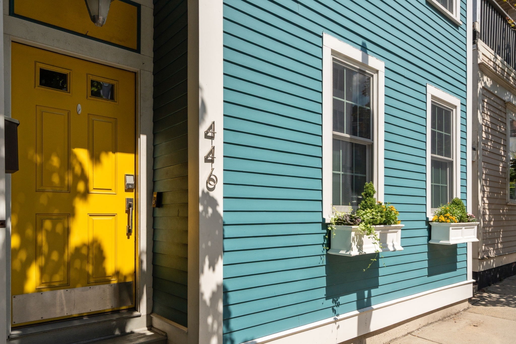 Turquoise house facade with a bright yellow front door and flower-filled window boxes.