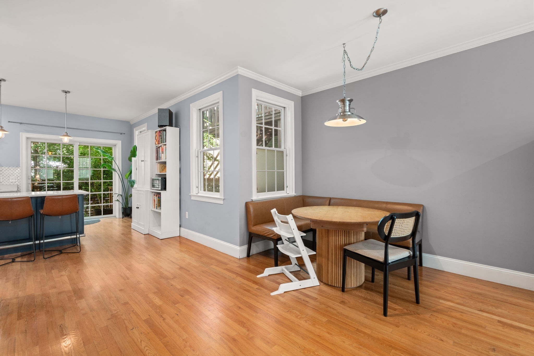 Dining area with a round wood table, built-in banquette, and windows beside the kitchen.