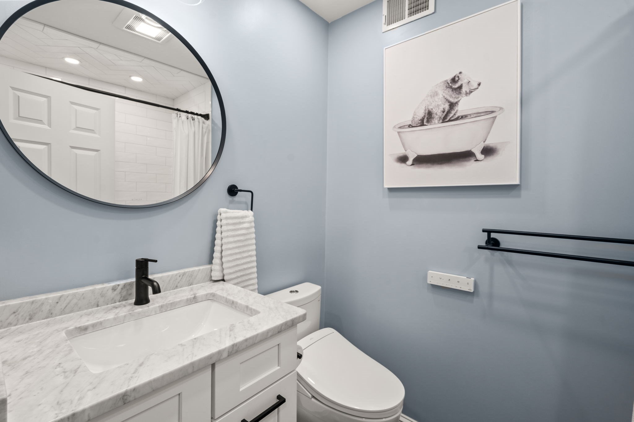 Bathroom with a marble-look vanity, oval mirror, and framed bear-in-a-bathtub artwork.