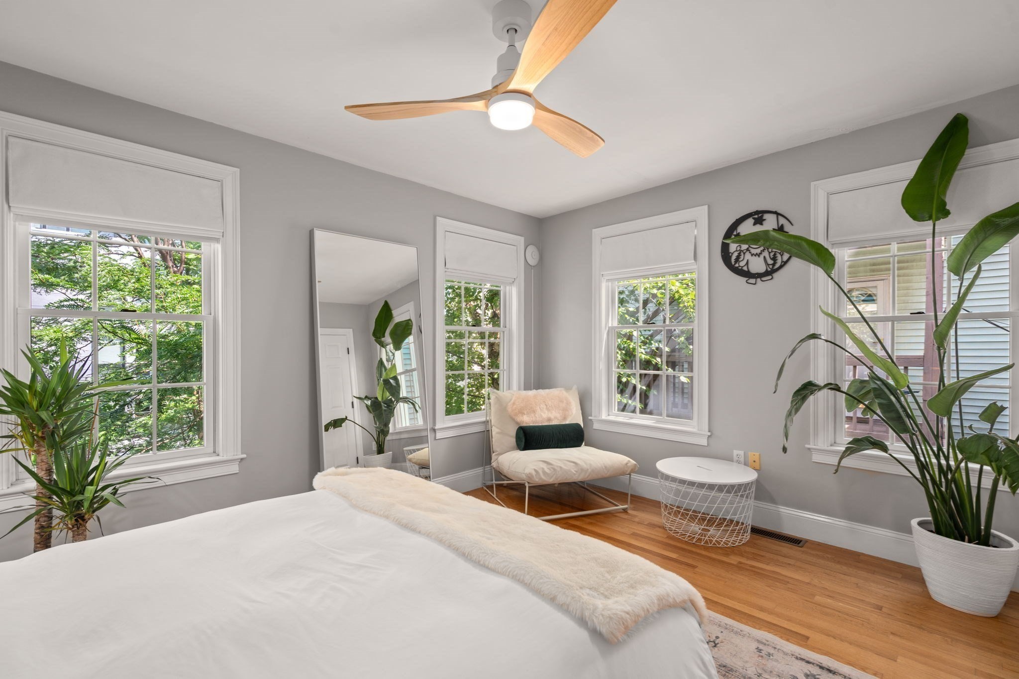 Bedroom with tall windows, hardwood floors, a ceiling fan, and leafy plants.