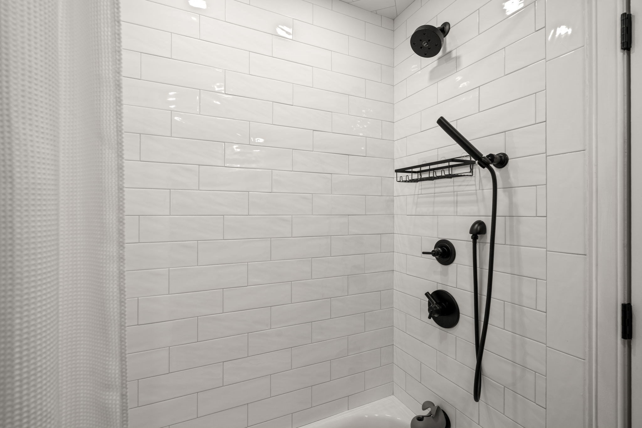 Tiled shower with matte black fixtures, handheld showerhead, and metal caddy.