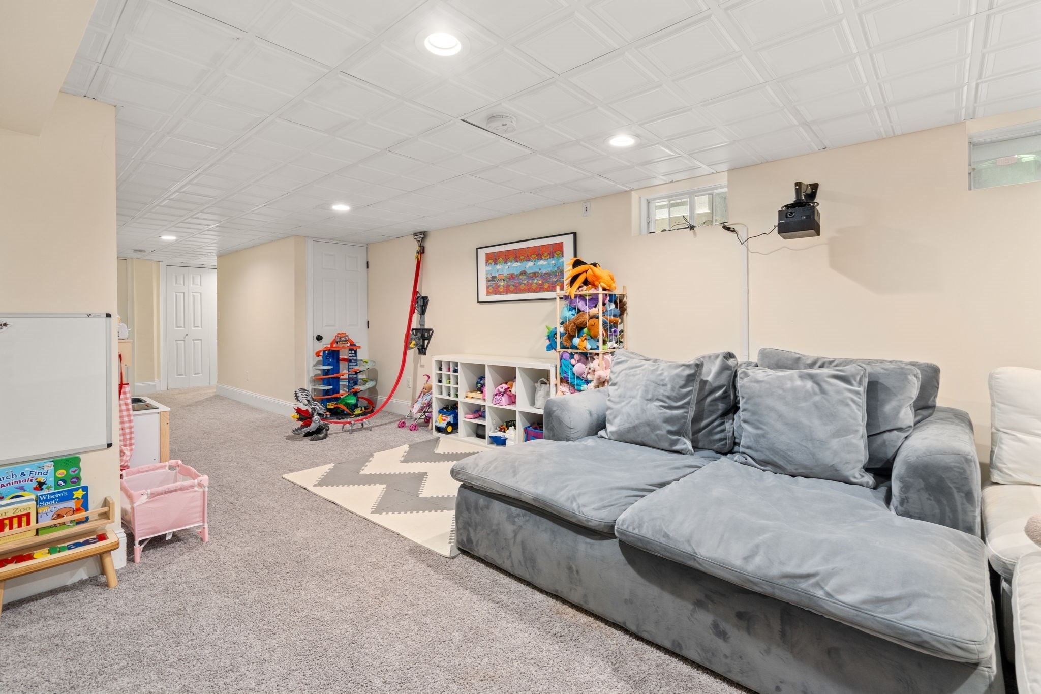 Basement playroom with a gray sectional, children's toys, and carpeted floor.