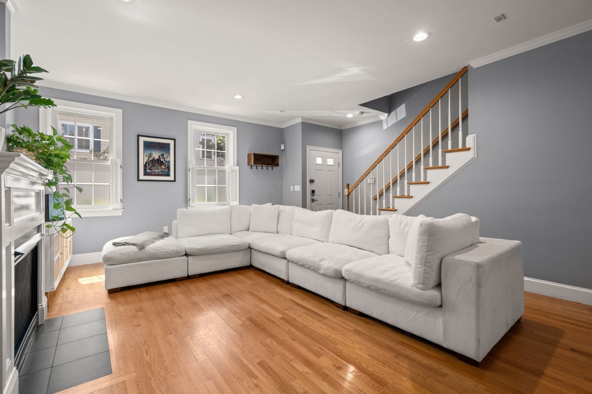 Living room with a white sectional, hardwood floors, fireplace, and staircase.