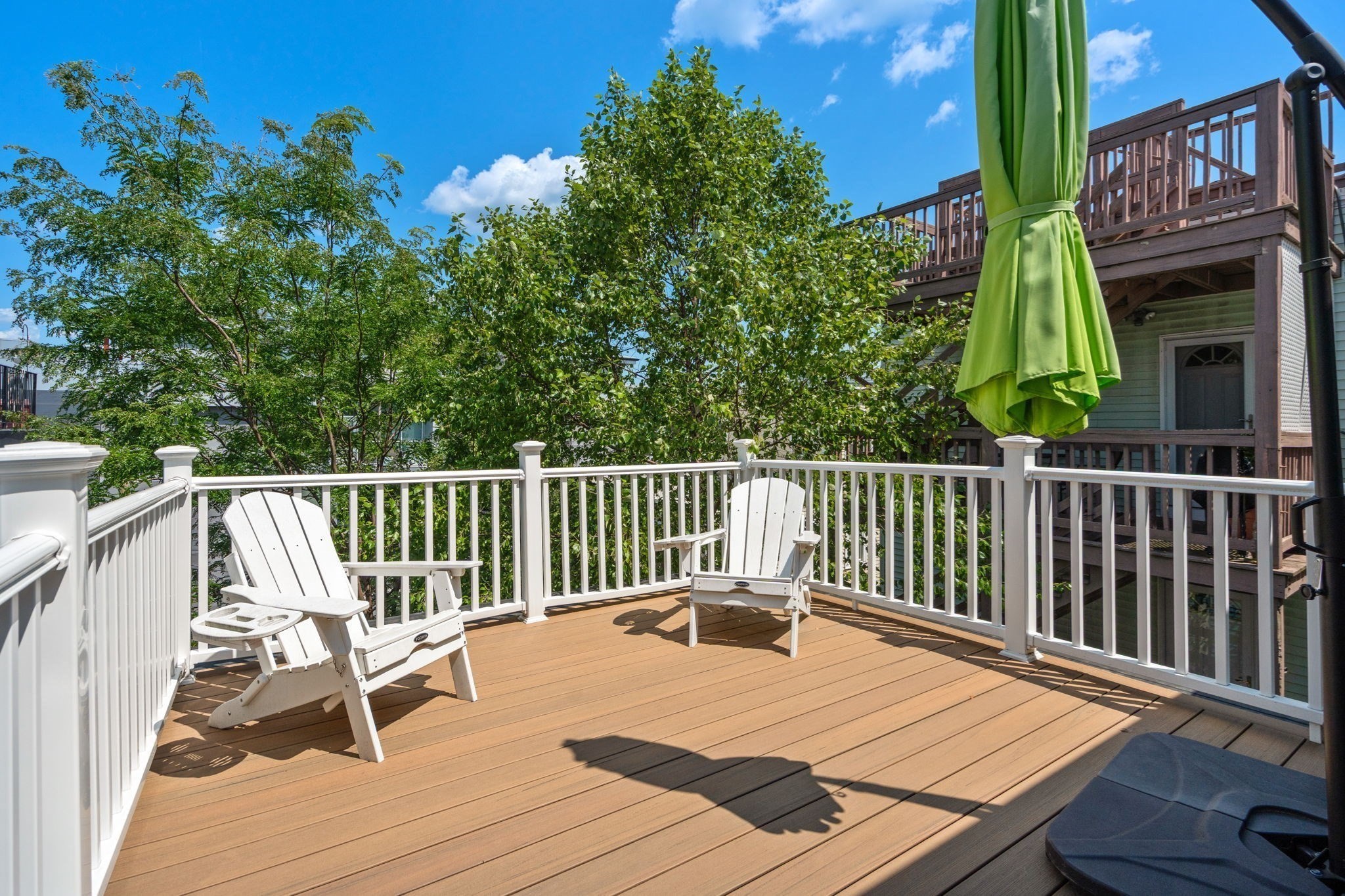 Deck with white Adirondack chairs, white railings, and a tied green umbrella.