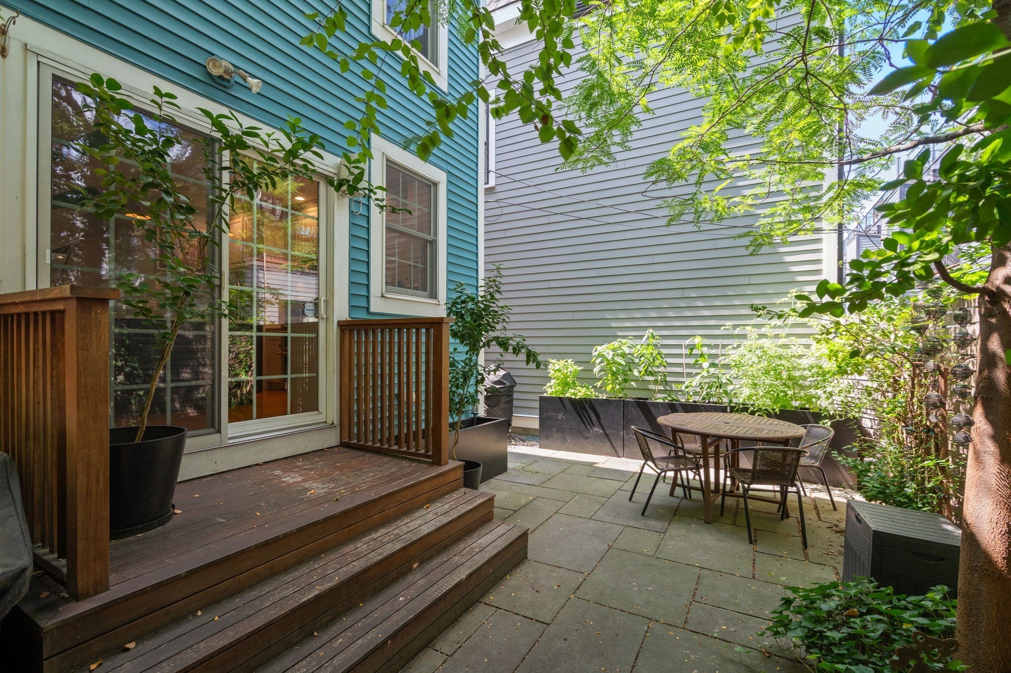 Private courtyard patio with wooden deck steps, stone pavers, raised planters, and outdoor dining set.